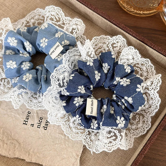 Two blue floral scrunchies on a lace doily with a 'Have a nice day' card.