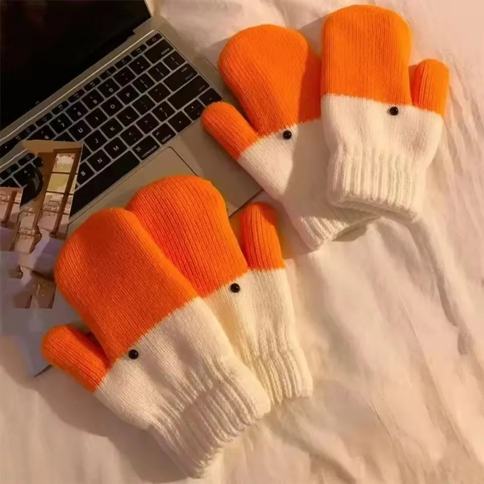 A pair of goose style knit split-color gloves with bright orange and white sections, styled on a white fabric surface next to a laptop.