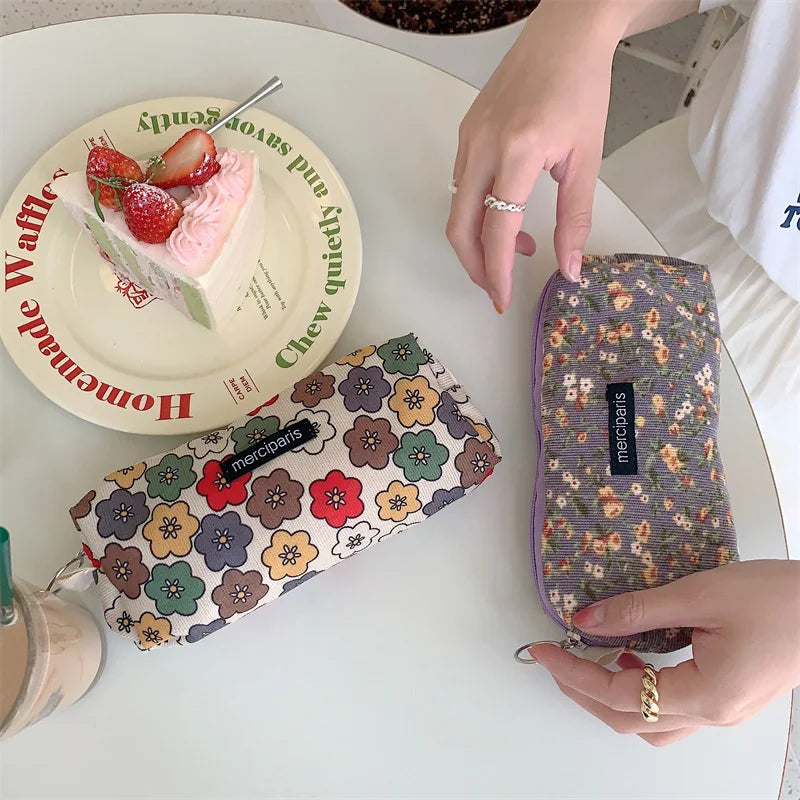 Two floral-patterned pouches on a table with a cake and a plate in the background.