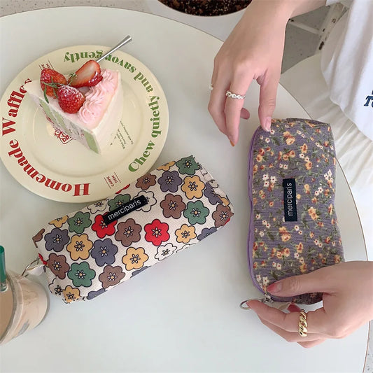 Two floral-patterned pouches on a table with a cake and a plate in the background.