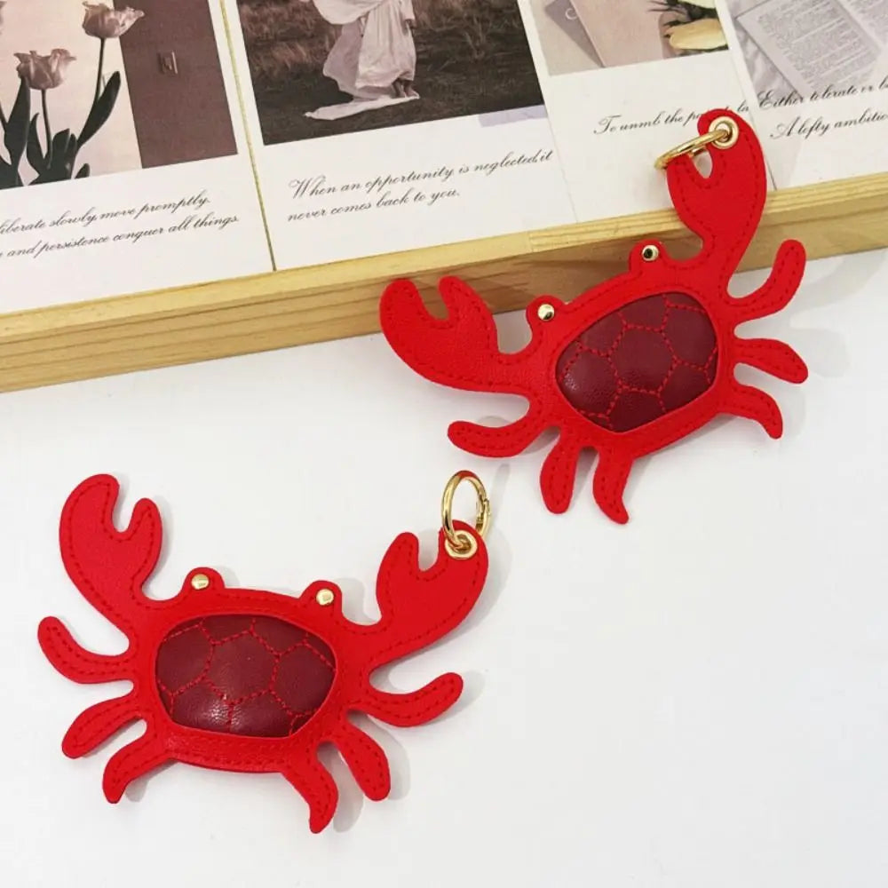 A pair of red felt crab-shaped earrings with gold-tone rings, displayed on a white surface with a decorative wooden card in the background.