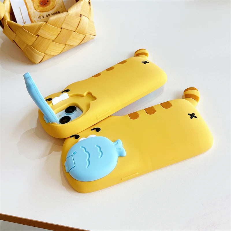 Two yellow cartoon phone cases with blue accents, featuring a cat-face design and a fish-shaped camera cover, displayed on a white surface with a woven basket in the background.
