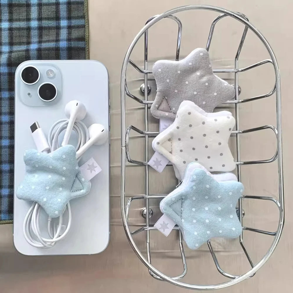 Three star-shaped fabric phone cable organizers in light blue, white, and gray are shown, with one holding a white phone and earbuds on the left, and two hanging on a metal wire rack on the right.