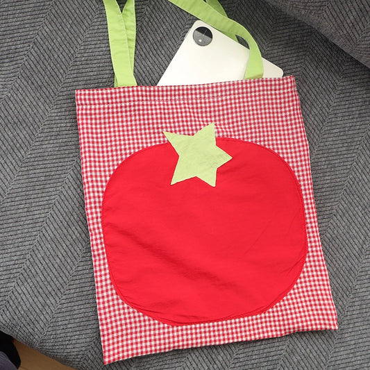 Red checkered bag with a red patchwork tomato on a textured gray surface