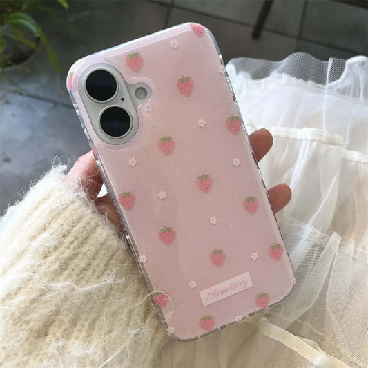 A hand wearing a cream-colored fuzzy sweater holds a clear phone case decorated with pink strawberries and small white flowers on a light pink background. The case has a small white label near the bottom that reads 'Strawberry'.