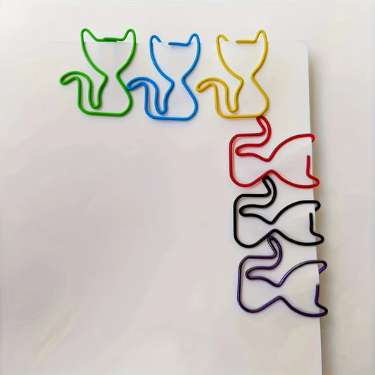 Five cat-shaped metal paperclips in green, blue, yellow, red, black, and purple, arranged on a white sheet of paper.
