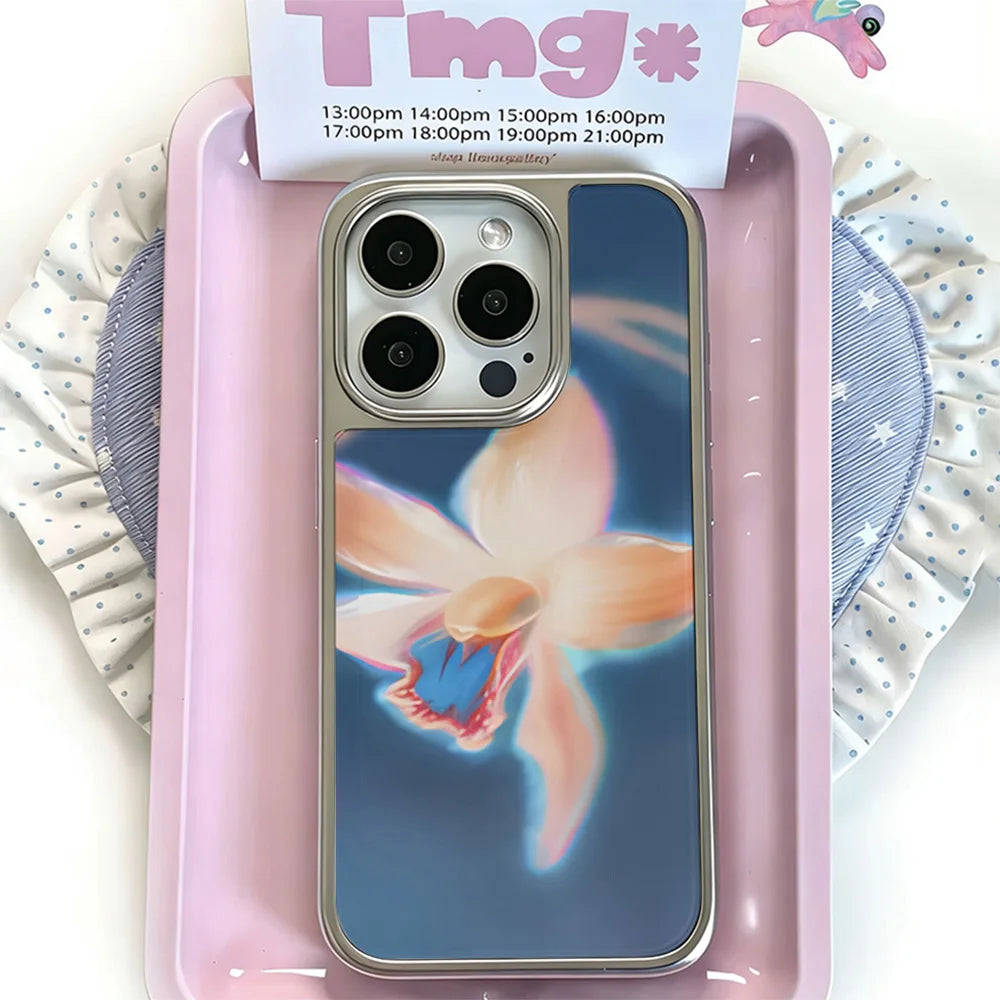 A phone case with a blue background and a large pink and orange flower graphic, shown in a pink tray with a card in the background.