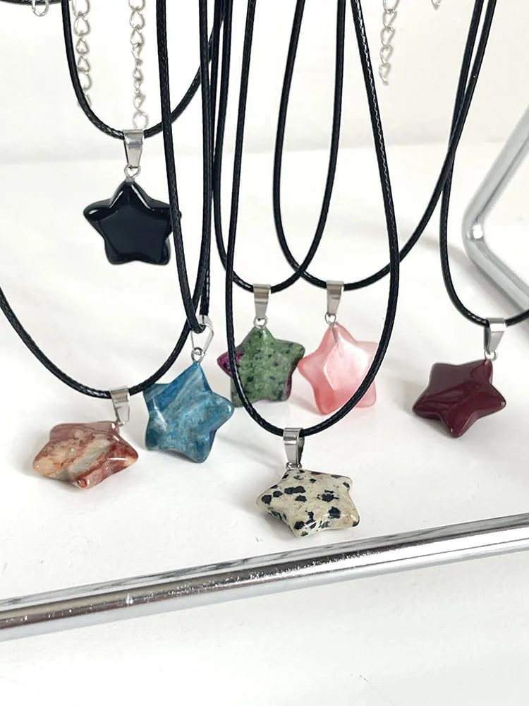 Star-shaped stone pendants on black cord necklaces displayed on a stand.