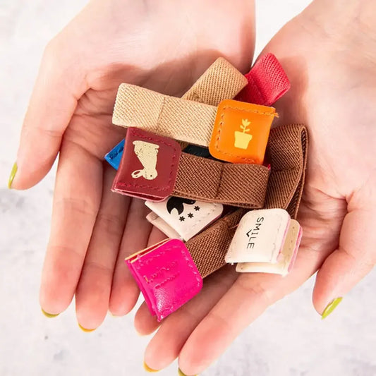 A pair of hands holding a small pile of cable tidies with different printed designs, photographed against a light marble-like background.