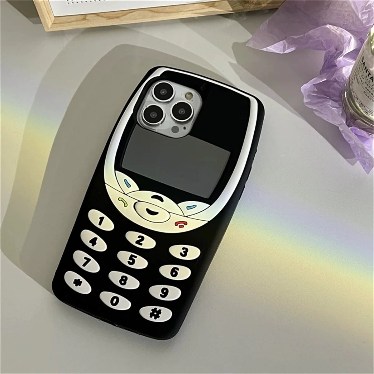 Phone case designed like an old-fashioned black phone with a rainbow effect on a light surface.