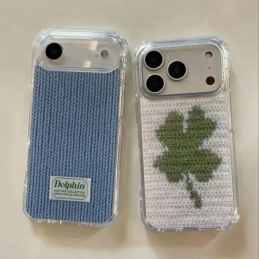Two clear phone cases with knitted back designs, one in light blue with a white Delphin label and one in white with a green shamrock, shown on a light beige background.