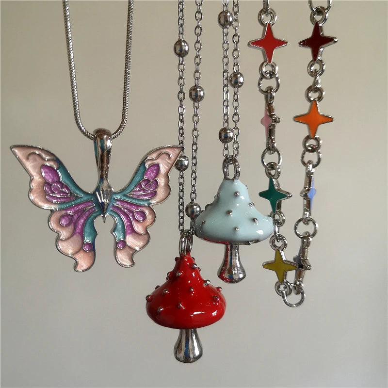 A set of colorful fantasy-themed necklaces hanging from silver chains against a plain light background. The necklaces feature a pink and purple butterfly pendant, a red mushroom pendant, a light blue mushroom pendant, and star-shaped links in red, orange, green, and yellow.
