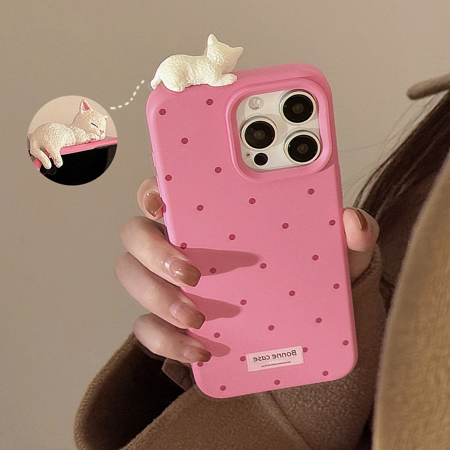 Pink polka dot phone case with a small white cat figure held by a person.