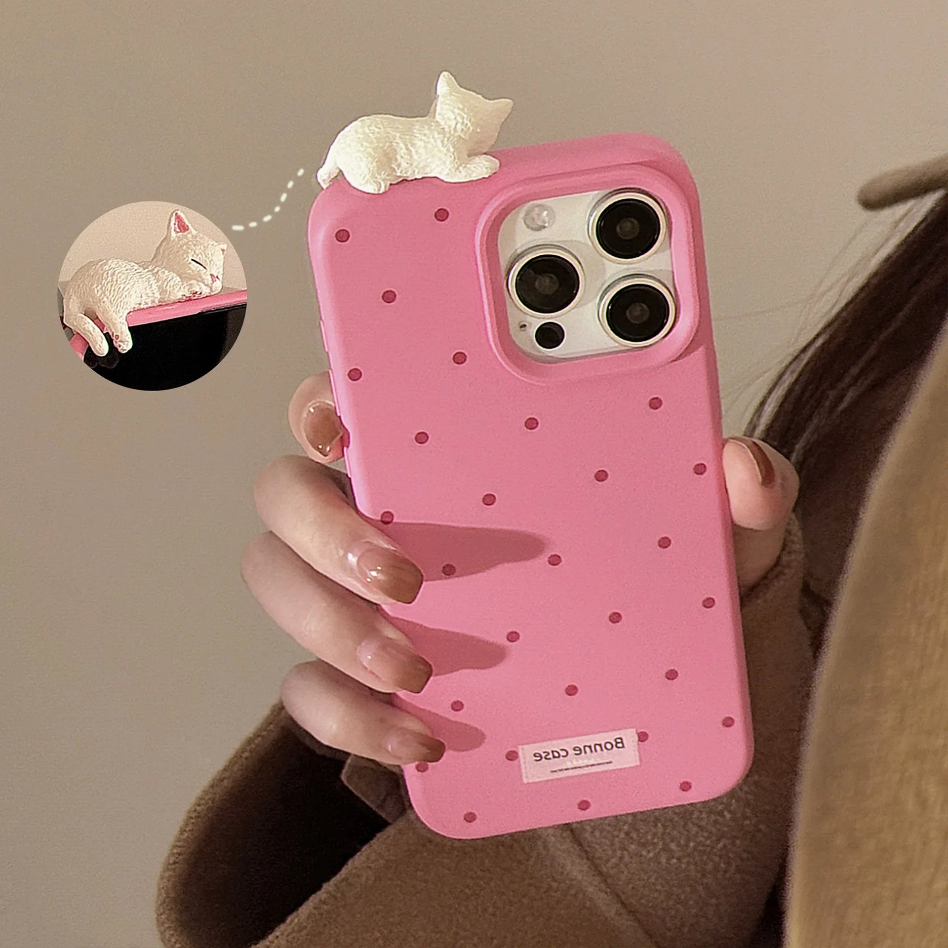 Pink polka dot phone case with a small white cat figure held by a person.