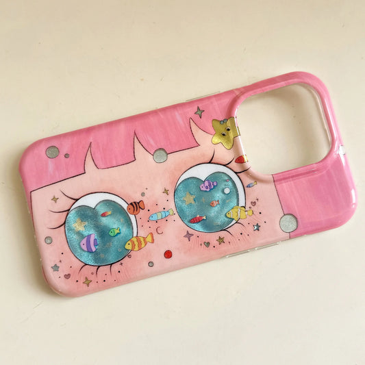 A pink phone case with a whimsical cartoon design featuring two large eyes, colorful fish, and stars, photographed on a light beige background.