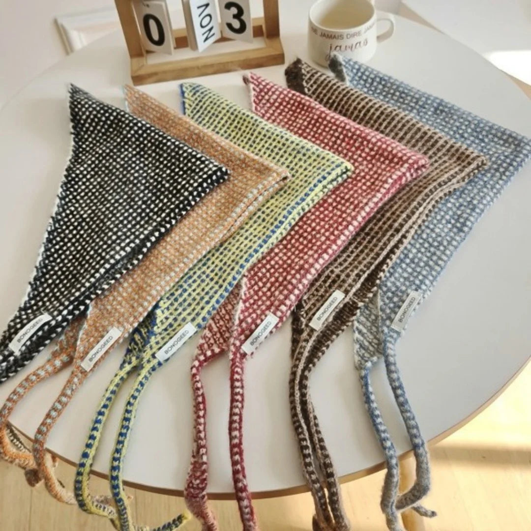 Six triangular woven bandanas in assorted earthy colors are arranged in a fan shape on a round white table. The bandanas include black and white, tan and beige, olive green and yellow, dusty pink and red, brown and cream, and blue and white.