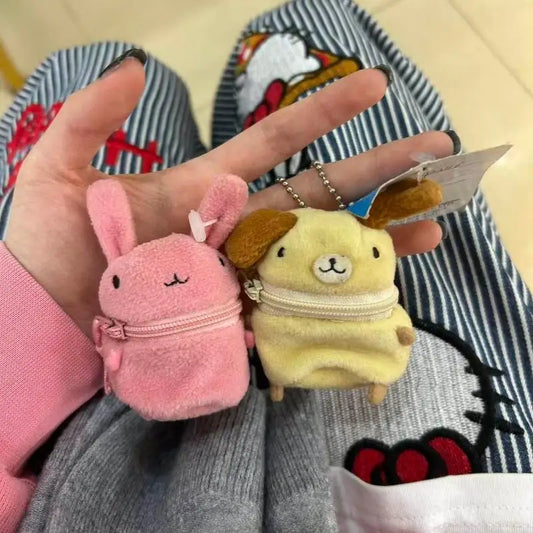 Two small plush character zip pouches held in a hand. One is pink with a bunny face and bow, and the other is pale yellow with a dog face and brown ears.