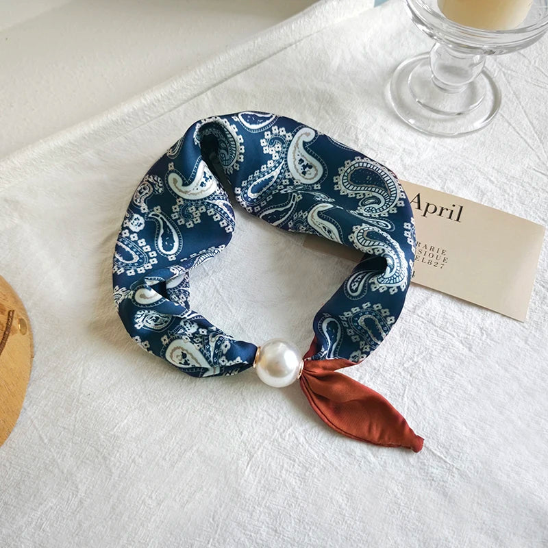 Blue paisley patterned scrunchie with a pearl and red ribbon on a white surface.