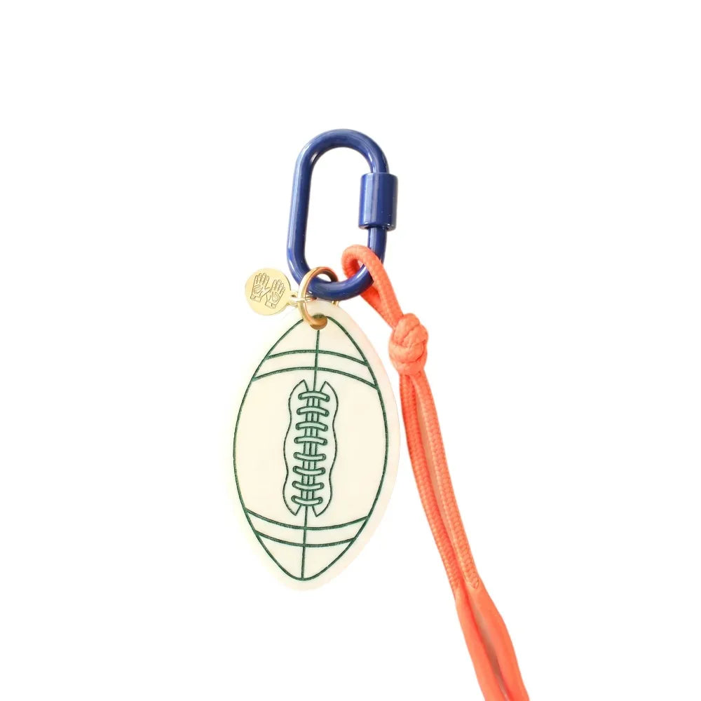 A football-shaped keychain or bag charm with a blue carabiner, orange cord, and a small gold tag on a plain white background.