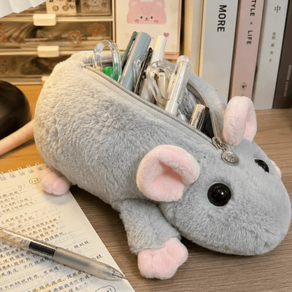 A gray plush mouse-shaped zipper pouch filled with pens and pencils, placed on a wooden desk with books and stationery in the background.