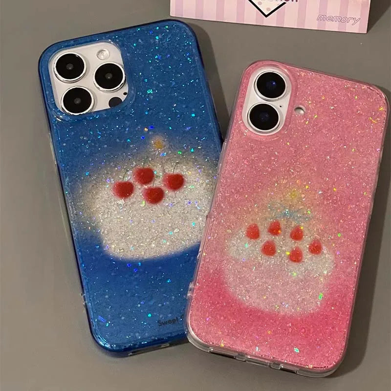 Two glittery phone cases shown on smartphones, one blue and one pink, both with a white cloud-like graphic and small red heart details, photographed on a gray surface.