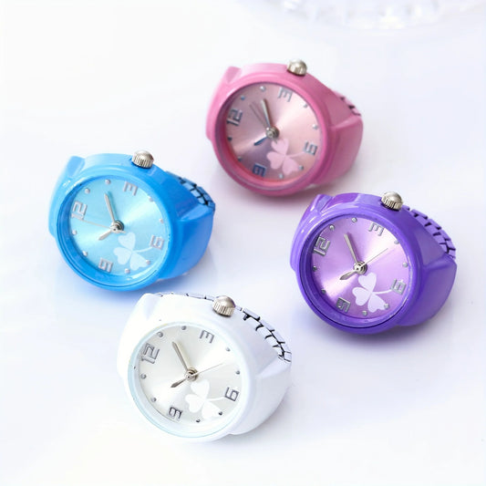Four retro-style wristwatches with round faces and matching colored straps, arranged on a white background. The watches are white, light blue, pink, and purple, each featuring a clover motif on the dial.