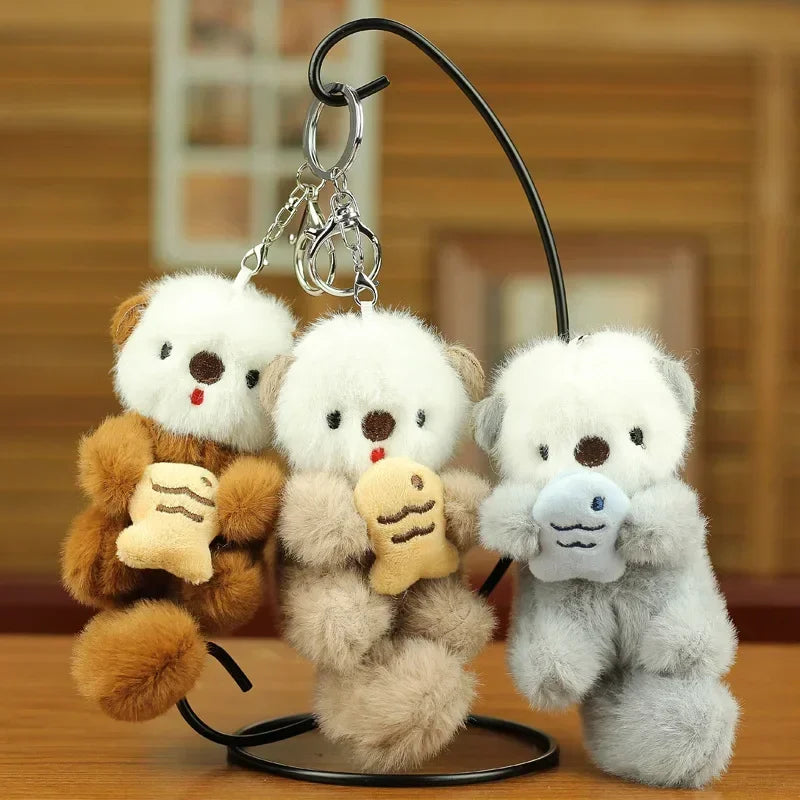 Three plush otter keychains on a stand with a wooden background