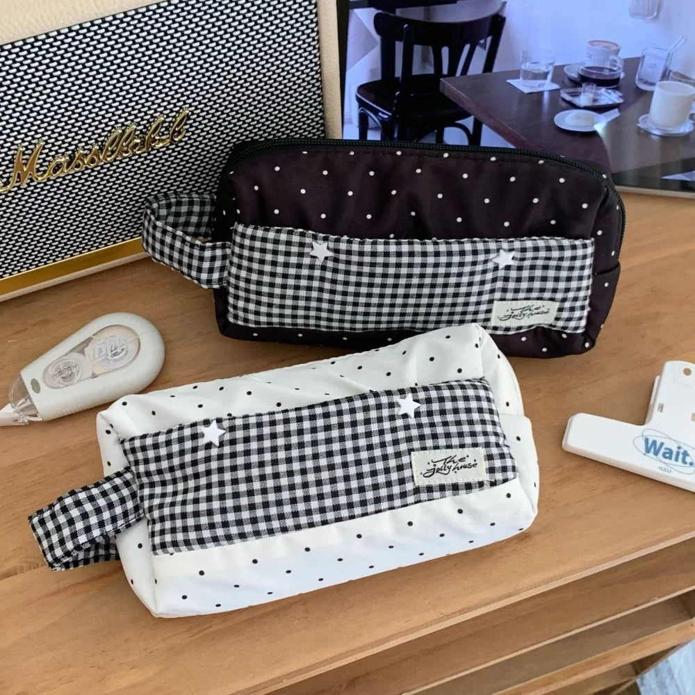 Two fabric pencil cases on a wooden desk, one black and white gingham with white polka dots and one white and black gingham with white polka dots, both featuring a small white embroidered bunny and a fabric label.