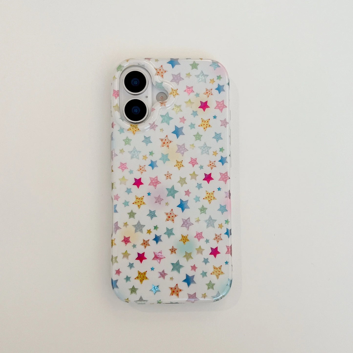 A clear phone case with a colorful pattern of small stars in pink, blue, yellow, and green on a white background, shown on a phone against a plain white surface.