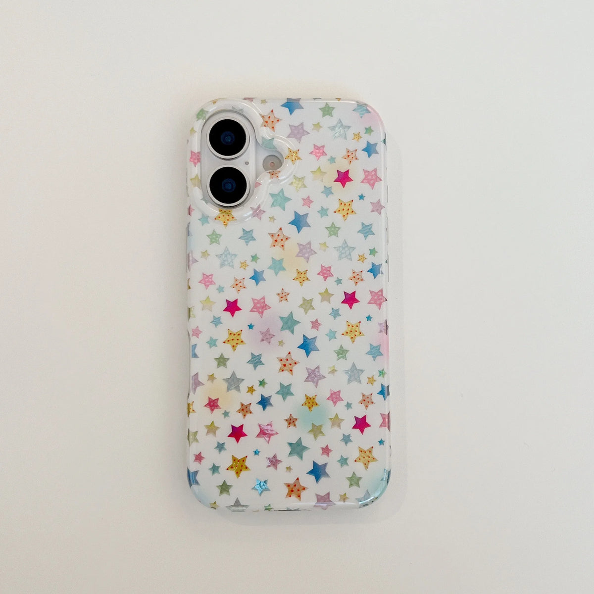 A clear phone case with a colorful pattern of small stars in pink, blue, yellow, and green on a white background, shown on a phone against a plain white surface.