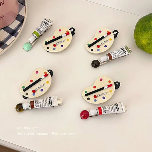 Set of small paint palette hair clips with paint tubes on a white surface