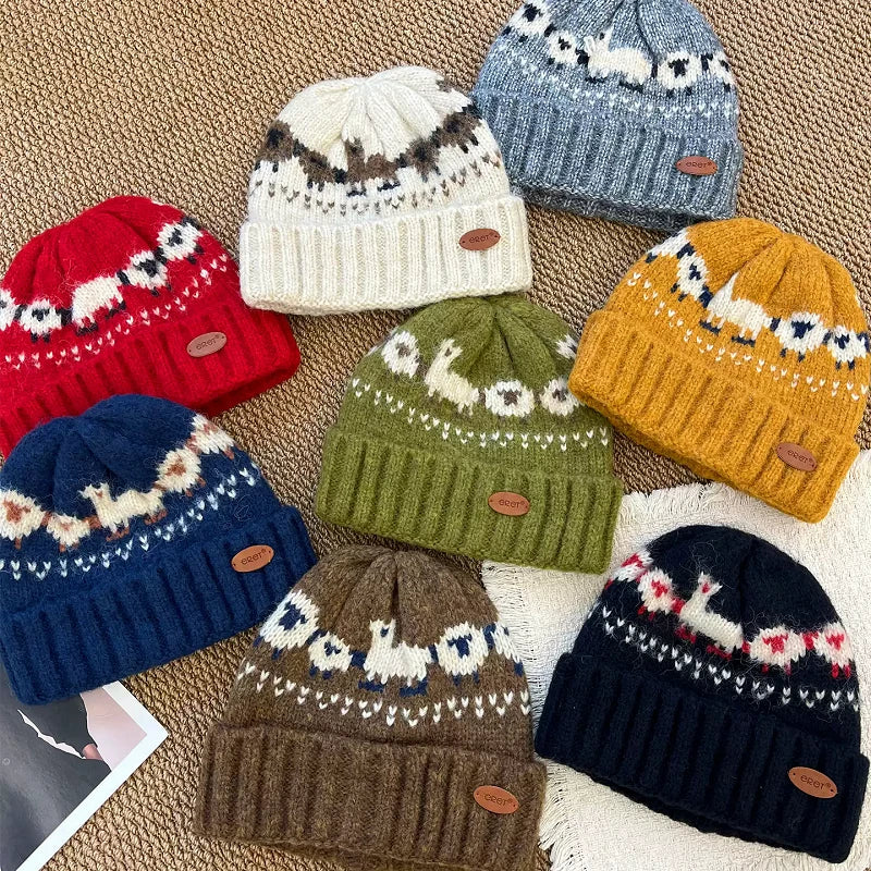 Seven knit beanie hats in different colors are arranged on a textured beige woven surface. Each hat has a Fair Isle style pattern near the top and a ribbed cuff, with a small brown leather patch.
