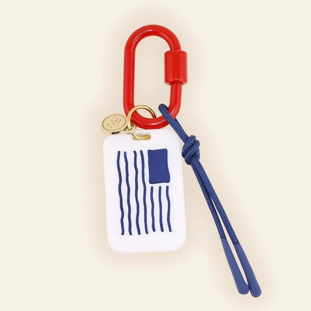 Keychain with red carabiner, white tag with blue stripes, and blue lanyard on beige background
