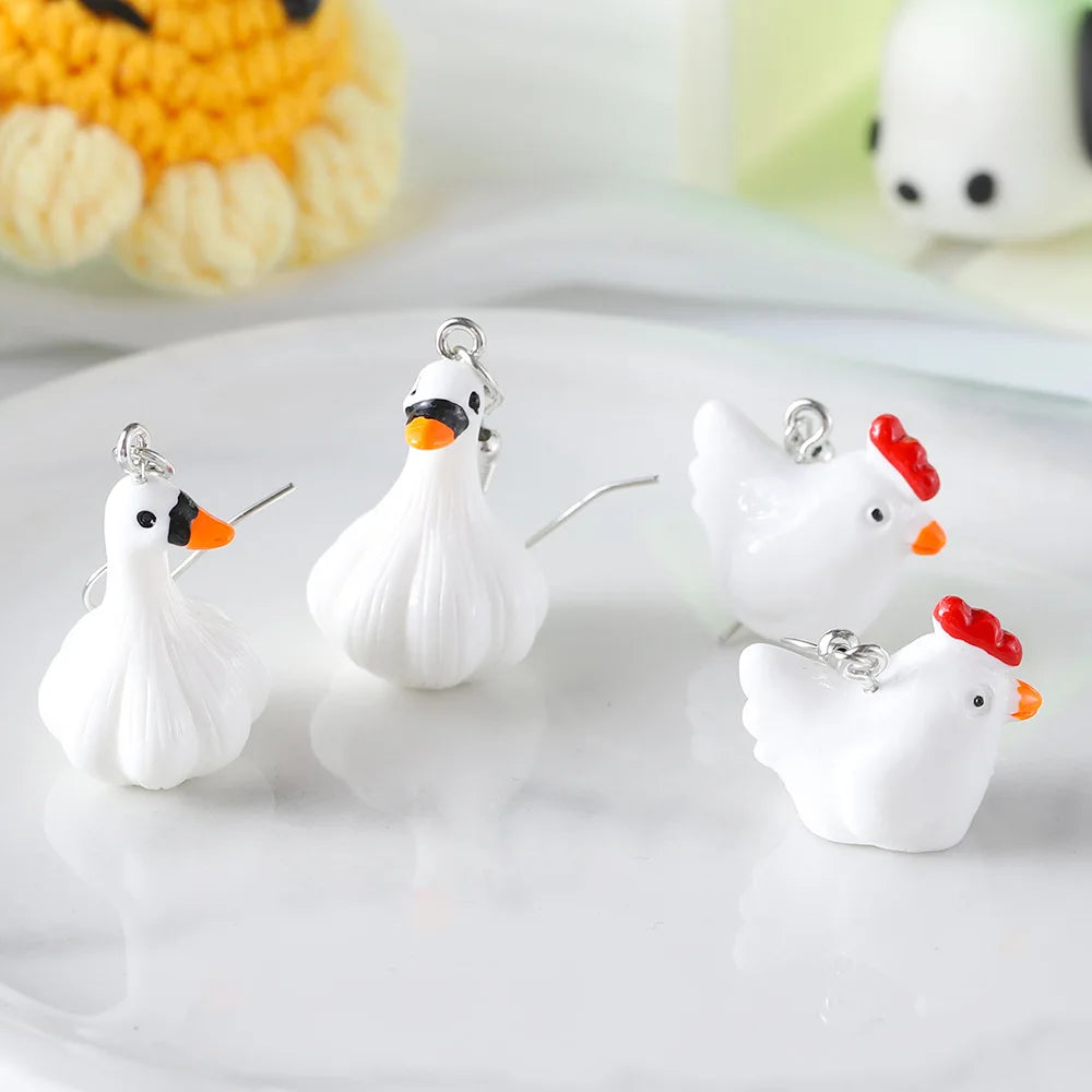 Set of four chicken-shaped earrings on a white surface with a blurred background.