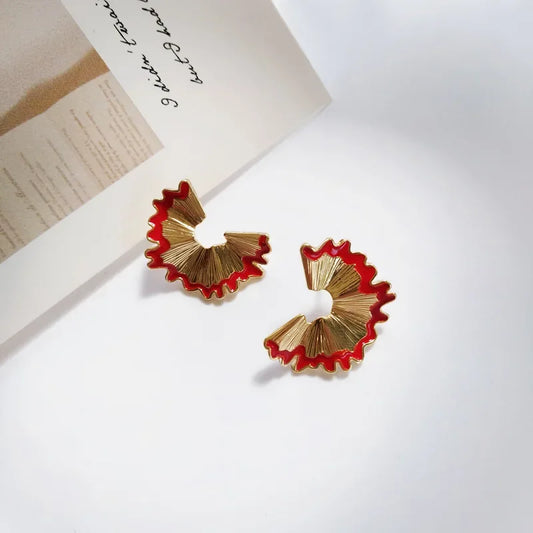 Gold and red earrings on a white surface with a piece of paper in the background.