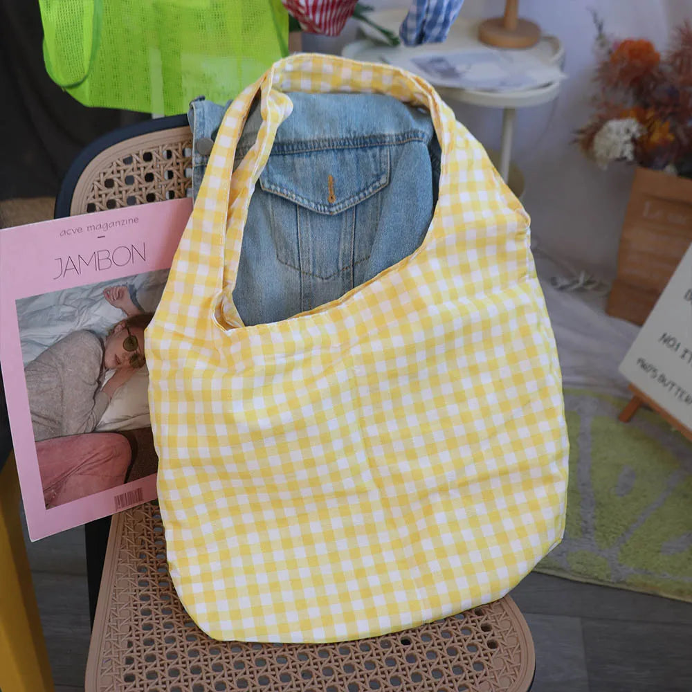 Yellow checkered bag with denim jeans inside, placed on a chair with a magazine and books around.