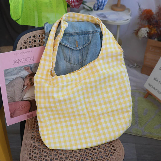 Yellow checkered bag with denim jeans inside, placed on a chair with a magazine and books around.