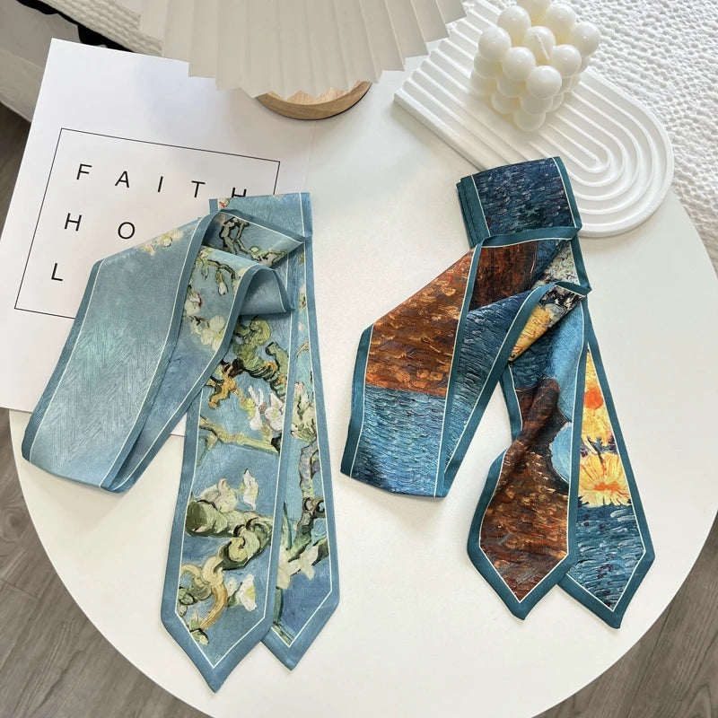 Two silk neckties with art-print designs are displayed on a white round table. The left tie features a light blue background with a floral pattern, and the right tie features a patchwork design of blue water, brown trees, and a yellow flower.