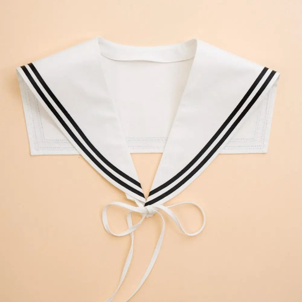 White sailor collar neck warmer with double black stripes and a white tie, laid flat on a light peach background.