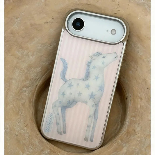 A phone case with a pale pink ribbed background, a light blue starry unicorn illustration, and a silver metallic bumper, shown resting in a textured beige stone bowl.