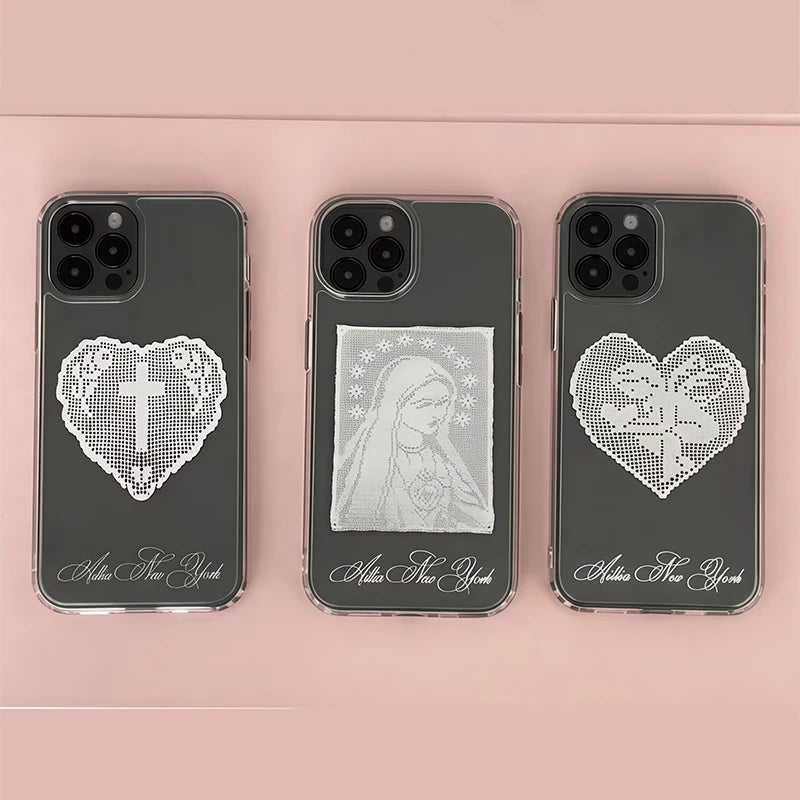 Three dark gray phone cases arranged side by side on a soft pink background. Each case has a white heart-shaped crystal or rhinestone design with a religious symbol in the center, plus white cursive text near the bottom.