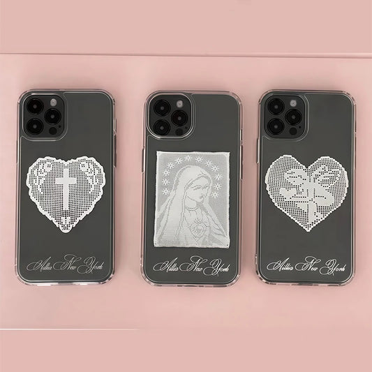 Three dark gray phone cases arranged side by side on a soft pink background. Each case has a white heart-shaped crystal or rhinestone design with a religious symbol in the center, plus white cursive text near the bottom.