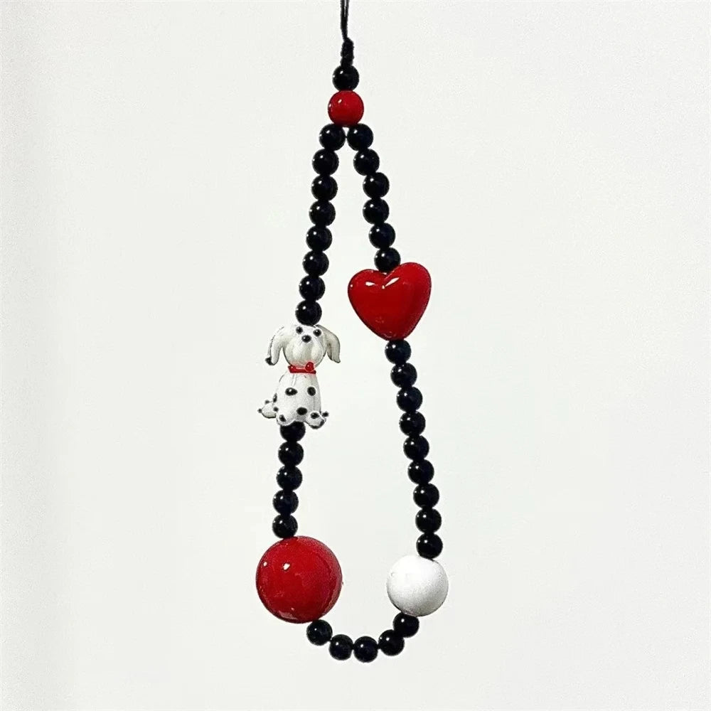A beaded hanging ornament or phone strap featuring black round beads, a glossy red heart, a white and black dalmatian figurine, and a large red oval bead on a plain light background.