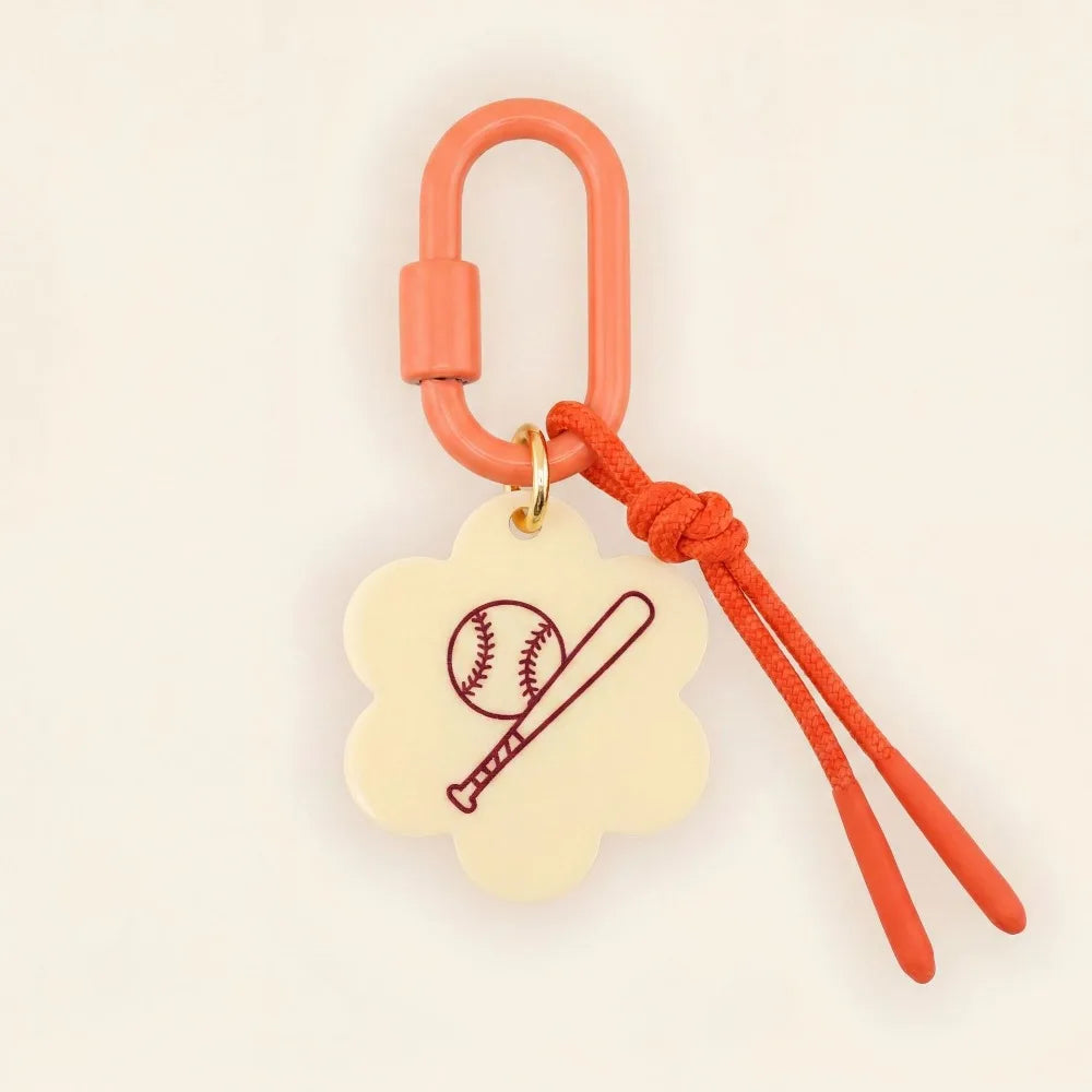 A baseball-themed keychain or bag charm featuring a cream-colored cloud-shaped tag with an engraved baseball and bat design, attached to a coral orange carabiner and matching cord.