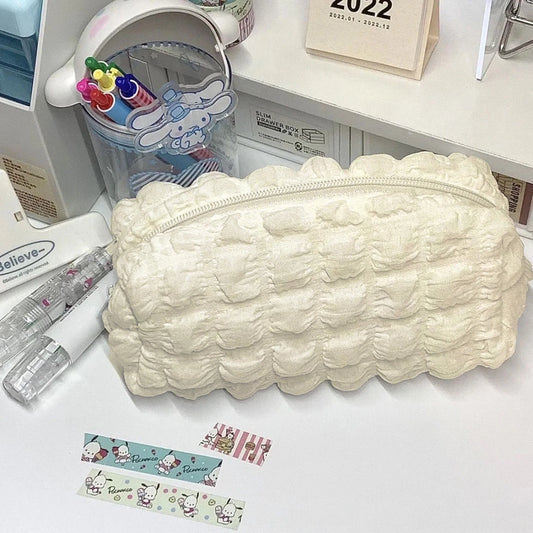 A cream-colored, textured bubble-patterned zippered pencil case or cosmetic pouch, displayed on a white desk alongside stationery items including washi tape, pens, and a Cinnamoroll-themed cup.