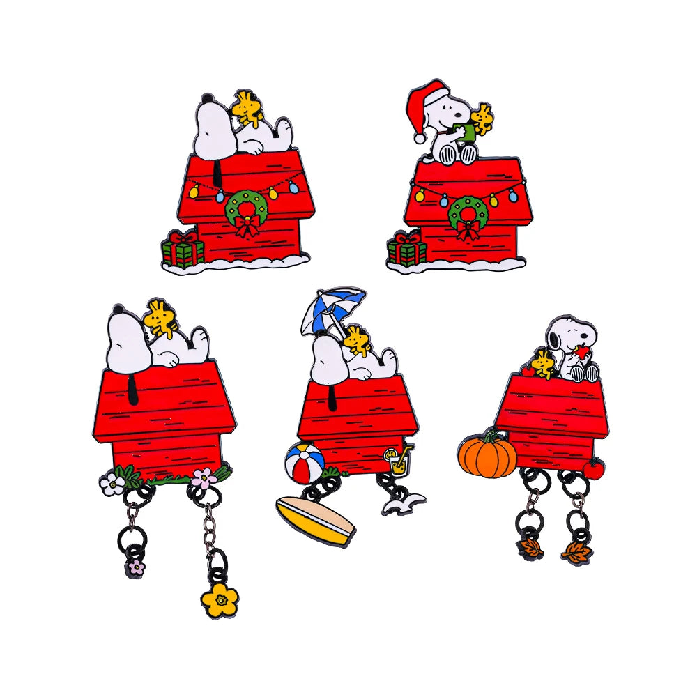 Five Snoopy and Woodstock holiday-themed enamel pins arranged on a white background, each mounted on a red doghouse charm with seasonal accessories like wreaths, gifts, a Santa hat, an umbrella, a pumpkin, and flowers.