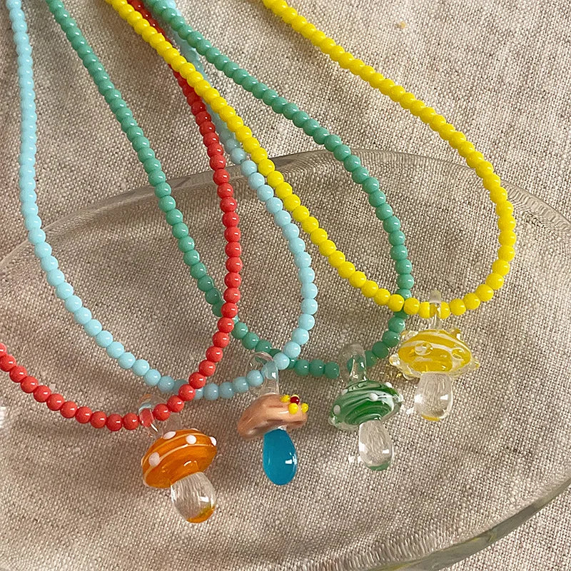Colorful beaded necklaces with mushroom charms on a textured surface