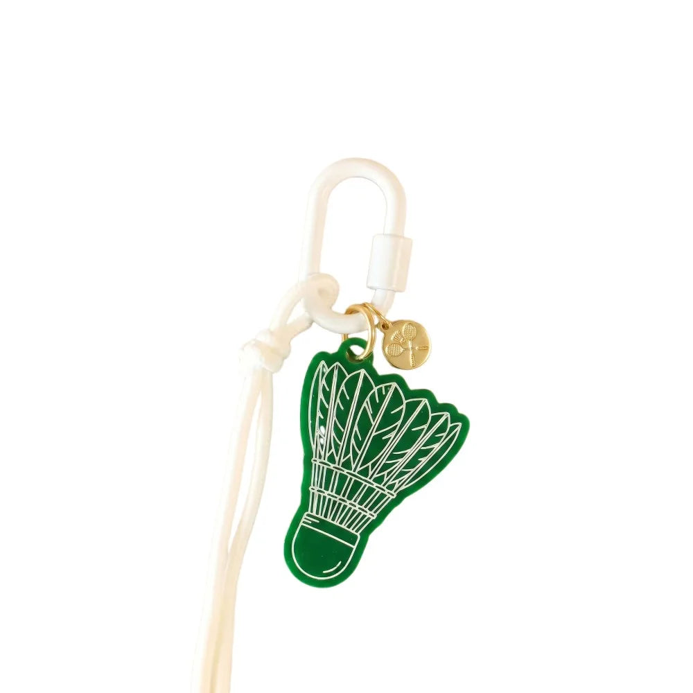 A green shuttlecock-shaped charm with white line art, attached to a white cord and white carabiner clip with a small gold round charm, on a plain white background.