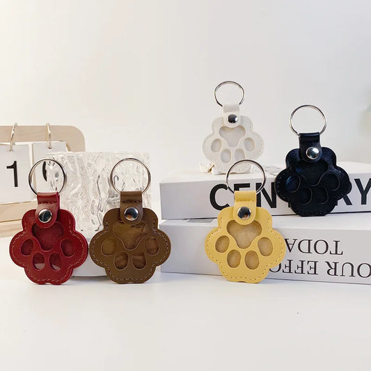Set of paw-shaped keychains in red, brown, yellow, and black on a white surface with books in the background.