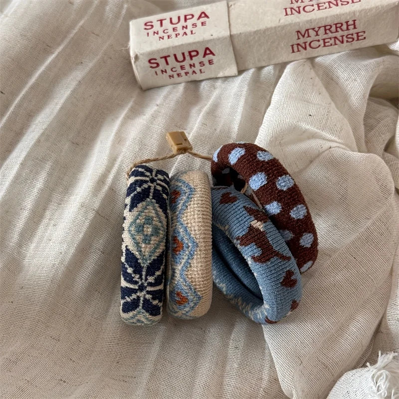 Three rolled incense sticks with geometric woven patterns in navy, cream, and brown with light blue dots, displayed on a textured off-white fabric next to their white paper packaging boxes labeled 'STUPA INCENSE NEPAL'.